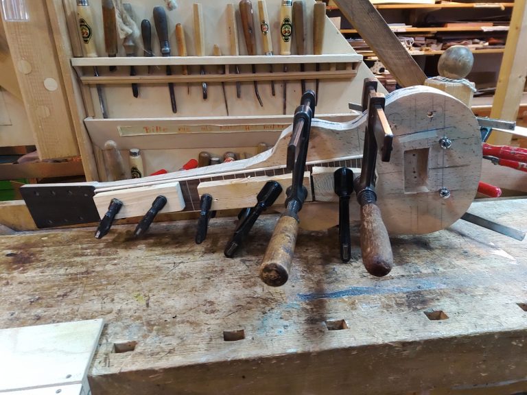 Werkbank mit einer Hawaigitarre, bei der das Griffbrett mit Zwingen festgeleimt ist