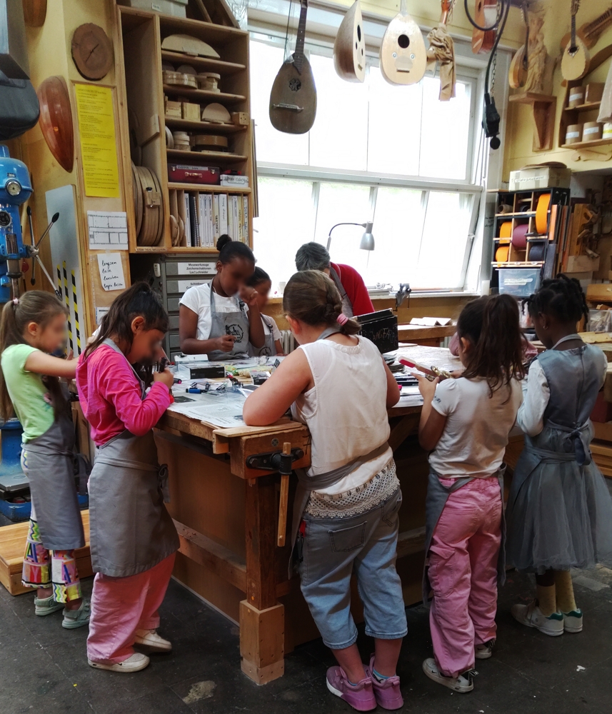 Kinder stehen um einen Tisch und malen in der Werkstatt